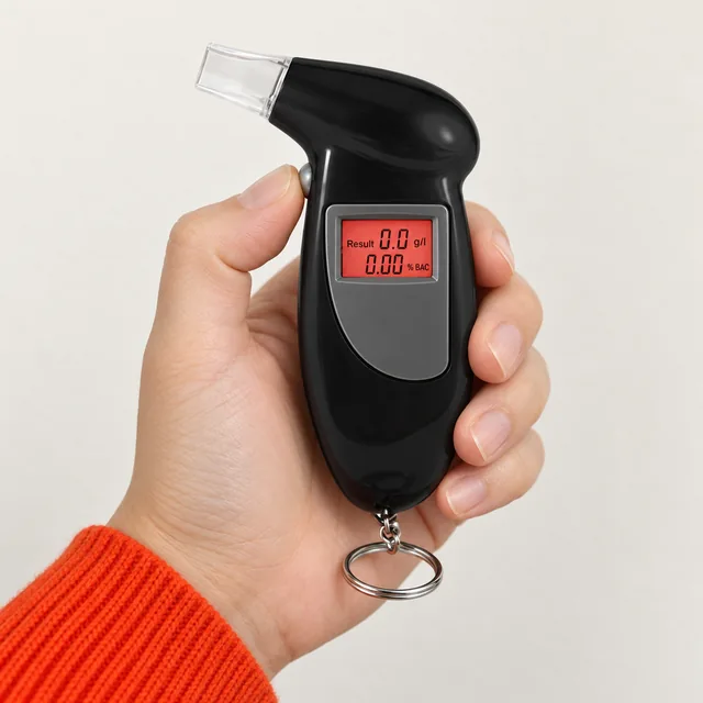 A hand holding the black AlcoGate, its clear mouthpiece at the top, its red display lit and its key ring below