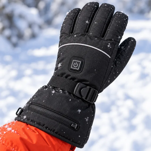 The back of a black AscentArc heated glove in the snow, its square power button, the white piping and the wrist strap in view