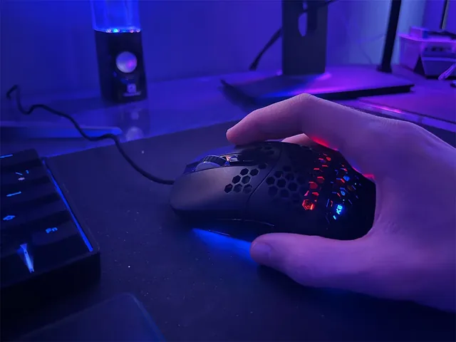 A hand on the AXEG Pro Mouse at a dark desk, its honeycomb shell lit red and blue from inside