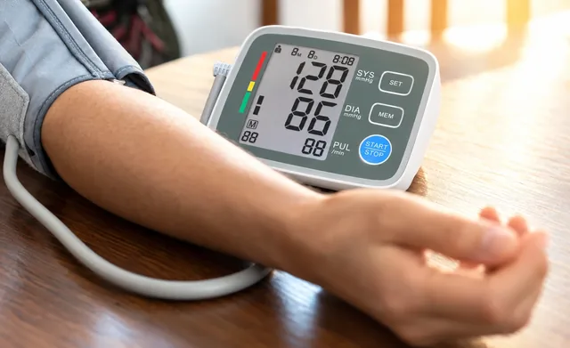 An arm resting on a wooden table in the gray cuff, the BP MeasureX beside it reading 128 over 86