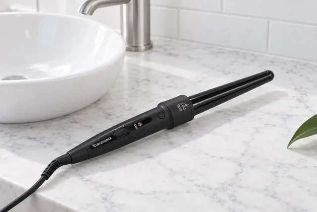 The Curlegance wand with its tapered barrel fitted, lying on a white marble counter beside a white basin, its cord trailing off