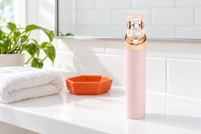 The EpiGlow standing with its cap on, on a bathroom shelf by a mirror, beside a folded towel, a soap dish and a small plant