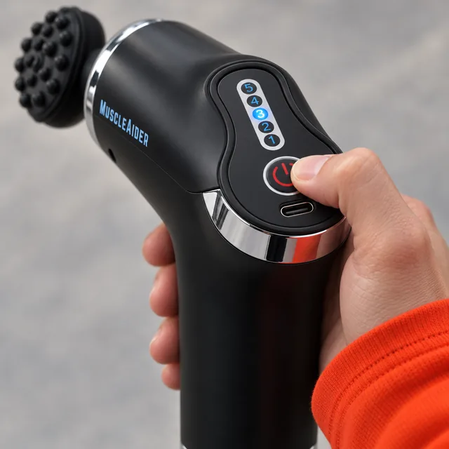 A thumb on the round power button at the back of the black MuscleAider, the five numbered speed lights above it and the USB-C socket below
