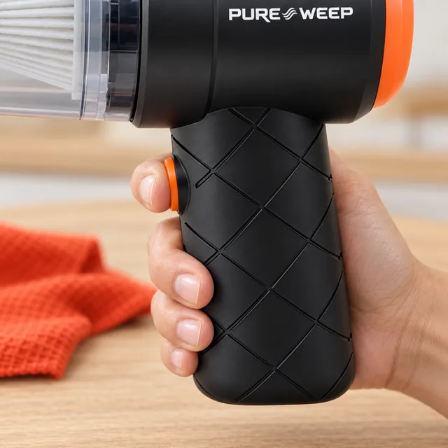 A hand on the diamond textured grip of the black PureSweep, a finger on its orange button