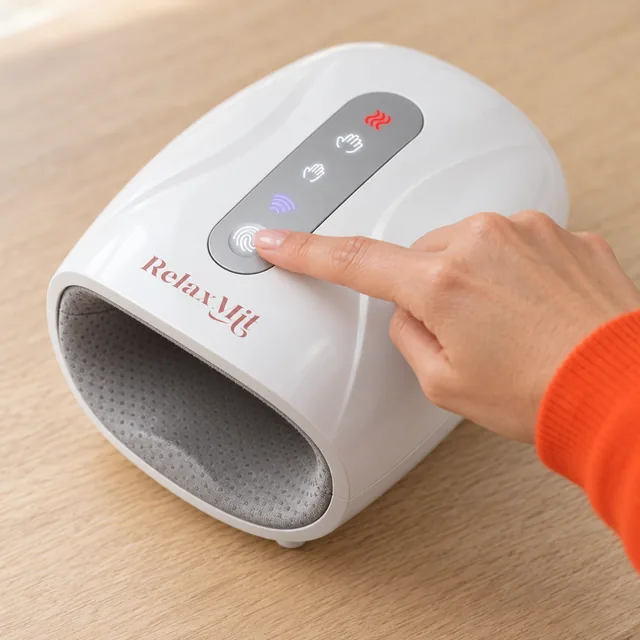 A fingertip on the round button at the end of the lit touch strip on top of the white RelaxMit, its icons glowing