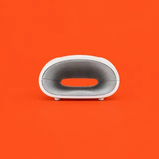 RelaxMit, the white hand massager seen from the front, its oval opening lined with gray dotted fabric, two small feet below, on a vermilion background