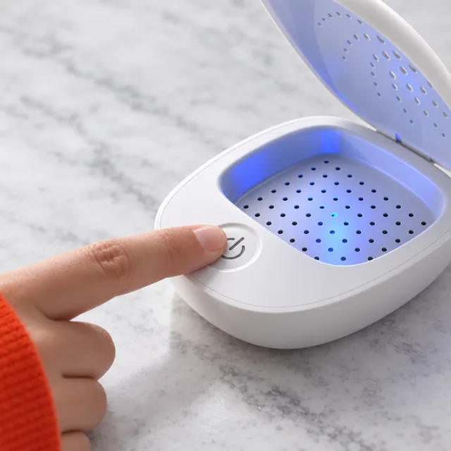 A fingertip on the round power button at the front of the open SereneDry, its chamber lit blue behind it