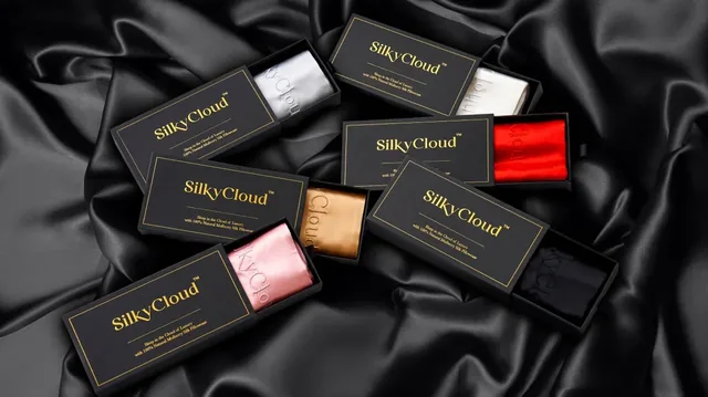 Six open black SilkyCloud drawer boxes on dark silk, each with the gold SilkyCloud wordmark and one folded pillowcase: silver, white, red, gold, pink and black