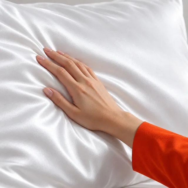 A hand gliding across the white silk of a Silky Cloud pillowcase, its sheen and soft folds in side light