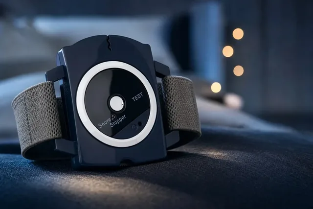 The SleepNix wrist unit on its gray strap, standing on a dark bed cover at night