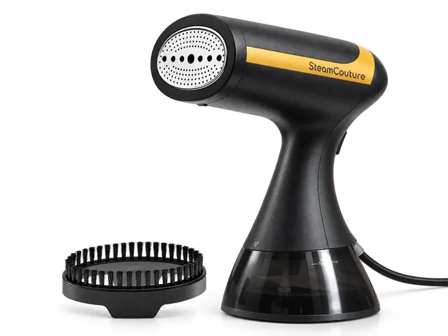 The black SteamCouture garment steamer with its gold band and white steam head, beside its round bristle brush head, on white