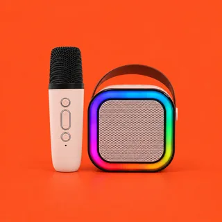VoxWizard, the small pale pink karaoke speaker with its rainbow light ring and brown strap handle, beside its wireless microphone with the black mesh head, on a vermilion background